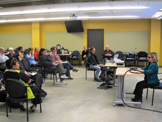 <p>
	Participants listen while Laura Mackenrot presents at a desk at the front of the room.</p>
