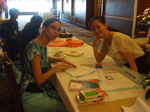 Mariam Ali and Chona Sabo sit and smile at a long table. 