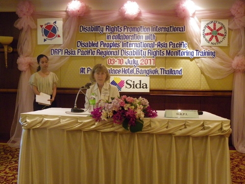 Marcia Rioux sits at a table and speaks into a microphone. 