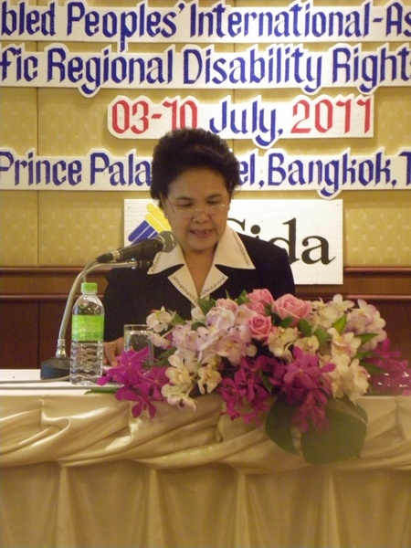 Ms. Kingkaew Inwang sits at a table and speaks into a microphone.