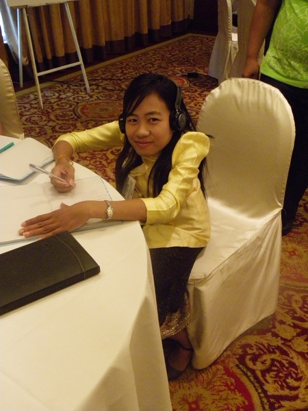 Phoutsady Laoly smiles and while sitting at a table and writing in a notebook. 