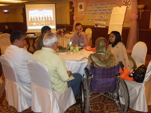 <p>
	Participants and facilitators sit and talk around a large round table.</p>
