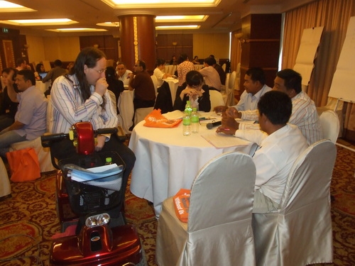 Co-facilitator Nathan (sitting in his mobility scoot) talks with participants at a table during the training. 