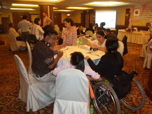 Chona Sabo stands beside a table of seated participants during training.