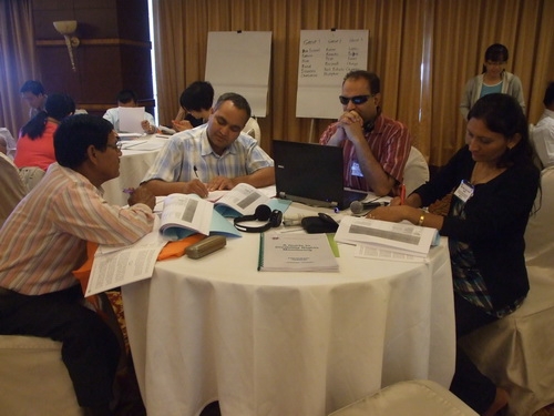 Ms. Ram, Mr. Birendra, Mr. Harka and Mr. Chintamani sit around a table working with training materials. 