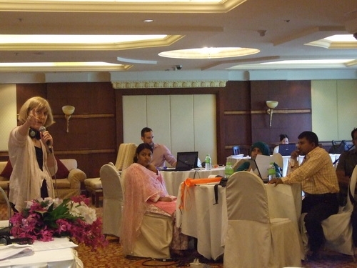 Marcia Rioux stands to the left and points to the camera while participants sit the right during training.