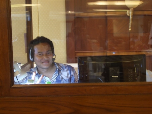 Sawang Srisom sits alone in an enclosed booth and smiles. 