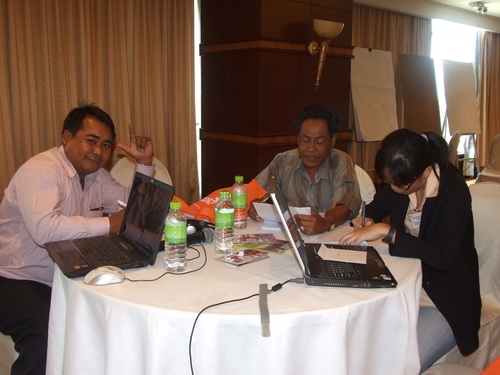 Soy Sokhorn, Prum and Channtey sit at a table and work with training materials. 