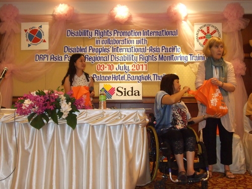 Marcia Rioux stands with her hand in an orange bag. Saowalak Thongkuay is looking into the bag and Chona Sabo looks on.