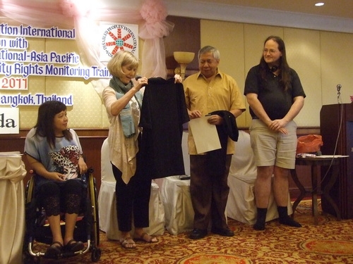 Lauro and Nathan stand while Marcia Rioux hands them t-shirts. Saowalak looks on.