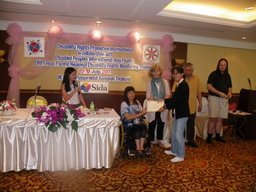 Channtey Heng smiles and holds her certificate with Saowalak Thonkuay while other facilitators look on. 