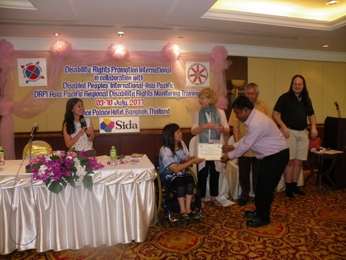 Soy Sokhorn smiles and holds his certificate with Saowalak Thonkuay while other facilitators look on. 