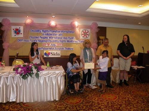 Phoutsady Laoly smiles and holds her certificate with Saowalak Thonkuay and Marcia Rioux while other facilitators look on. 