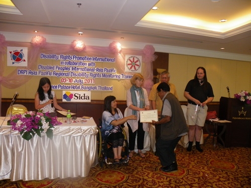 Chintamani Paudel holds his certificate and is congratulated by Saowalak Thonkuay and Marcia Rioux while other facilitators look on. 