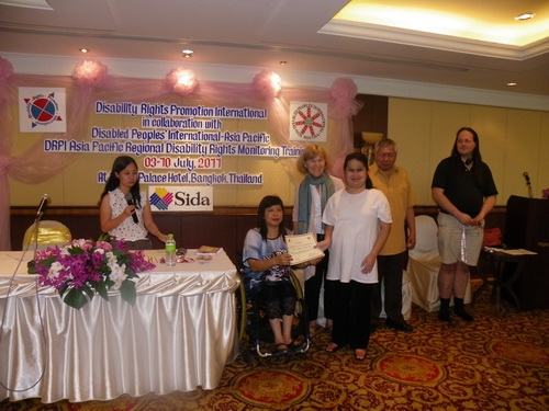 Krongkaew Jindapong smiles while holding her certificate with Saowalak Thonkuay while other facilitators look on. 