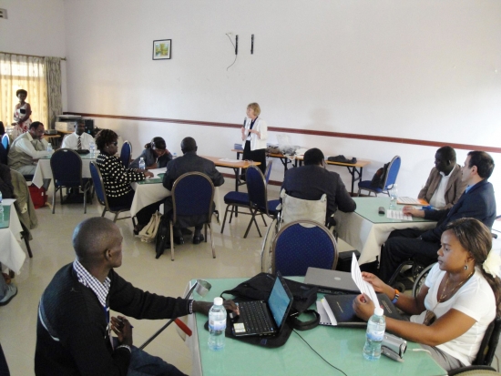 Marcia Rioux speaks into a microphone while participants sit at small round tables.