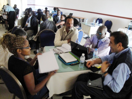 A woman and three men can be seen sitting around a table loaded with laptops and paper.