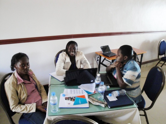 Three women sit around a table filled with laptops and training materials.