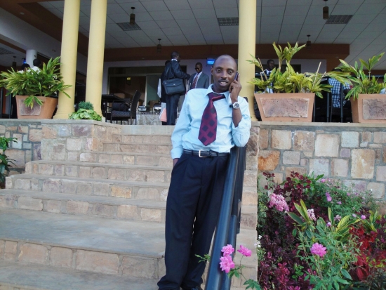 Mr. Ted Kaberuka talks on a phone while standing on stairs outside the hotel.