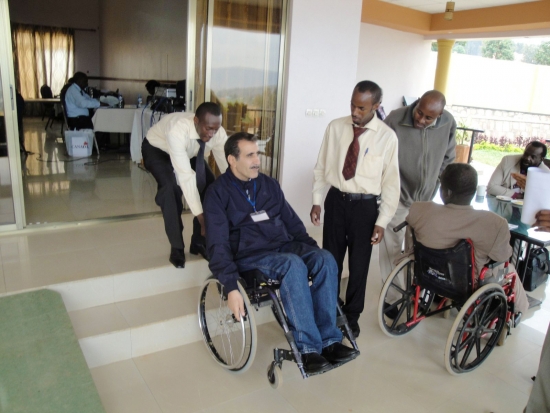 <p>
	A man pulls another in a wheelchair up a small section of stairs outside the training room while others watch.</p>
