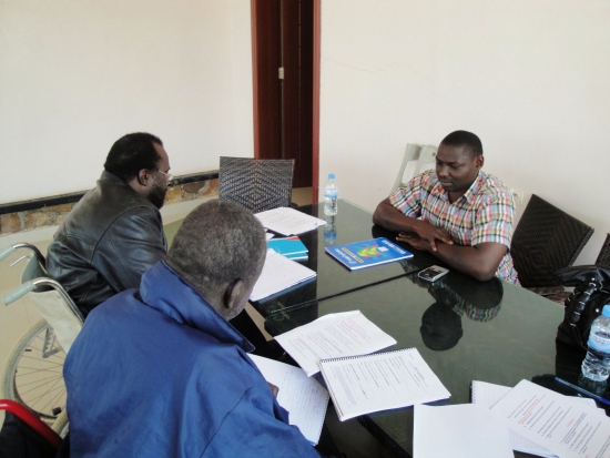 <p>
	Three men sit at a large shiny black table covered with training materials.</p>
