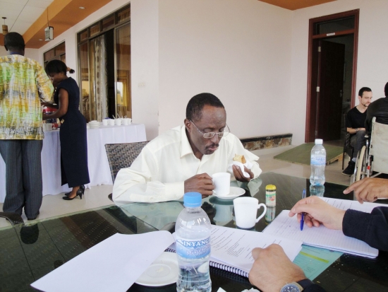 A man sits at a table with food in one hand and a cup in the other.