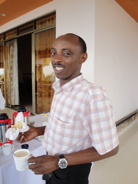 A man stands and smiles while holding food in one hand and a cup in the other