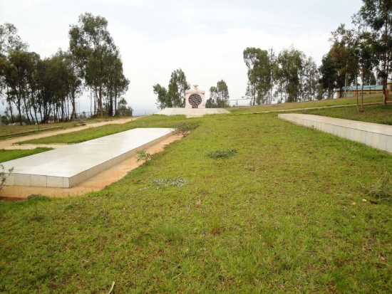 <p>
	A large grass covered area is shown with two large, white stone areas. In the distance a memorial marker and some trees can be seen.</p>
