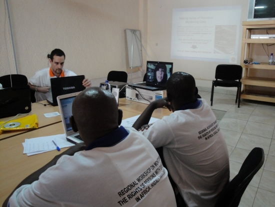 Severin Rwamucyo and Oswald Tuyizere look at a laptop with Paula Pinto's face on screen. Chris is also seen working on a laptop