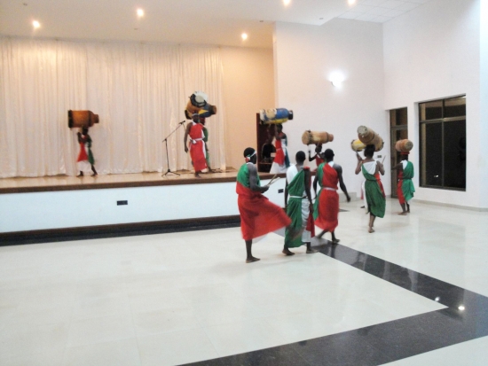 A line of drummers carrying drums walks onto a stage in a large white room
