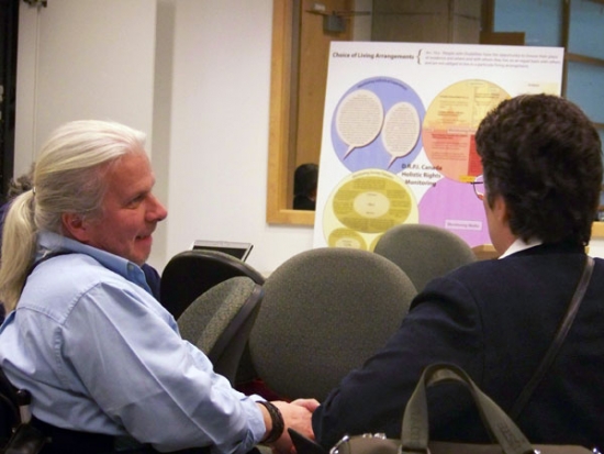 Normand Boucher is sitting while talking to an unidentified person.