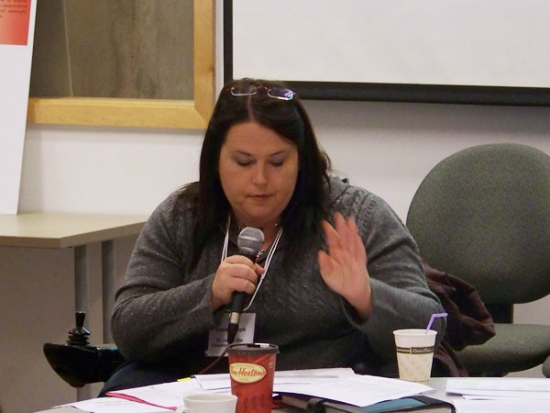 Susan Ralph is speaking into a microphone while looking down at a paper.