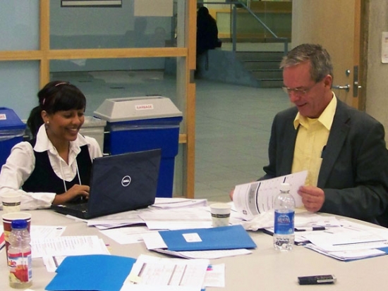 Two participants smile while working at a table littered with meeting papers.