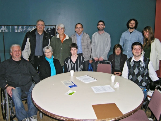 A group photo of the participants in the training seminar who are all standing behind a round table.