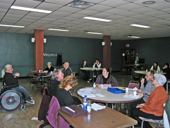 <p>
	Training participants sit around tables listening to Norman Boucher speak.</p>
