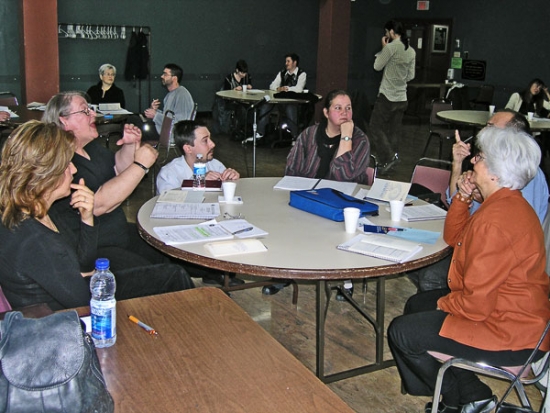 A group of training participants are talking while seated around a table. Other participants can be seen in the background.