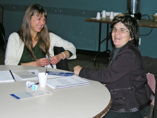 Catherine Fortier and Nathalie Nadeau both smile broadly while seated at a table.