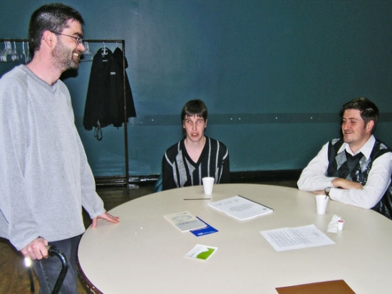 Simon Toulet stands while speaking with Lyne Robichaud and Jean-Michel Bernier (both seated at a table).