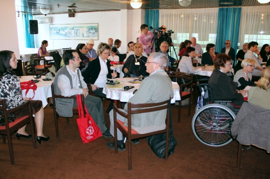 Training participants are seated around small tables. Video cameras on tripods can be seen in the background.