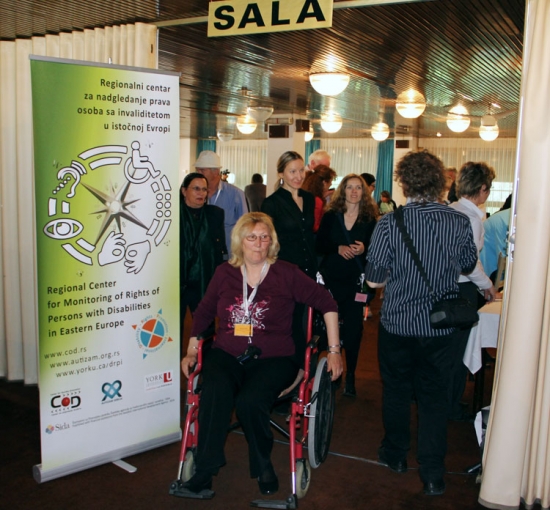 A crowd of people are close to the entrance to the training room. A large banner is located next to the entrance which reads 'Regional Center for Monitoring the Rights of Disabilities in Eastern Europe'.