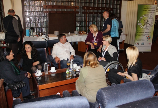 Seven training participants sit in comfortable chairs arranged around a coffee table and talk.