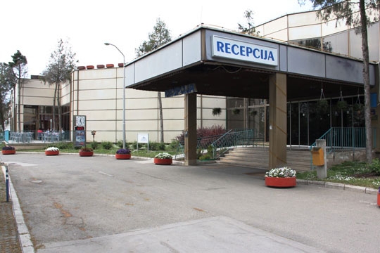 The entrance to the hotel is shown. A paved road leads up to the entrance over which a sign reads 'Recepcija'.