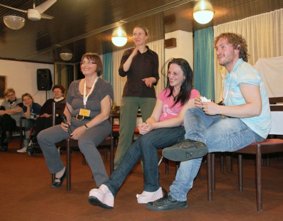 <p>
	Three participants (two females and one male) are seated in chairs and one woman is holding a microphone. A sign language interpreter stands behind them and signs.</p>
