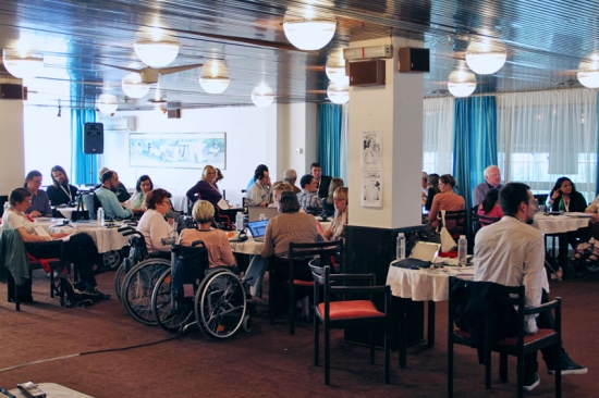 Many participants are arranged around tables in the training room.