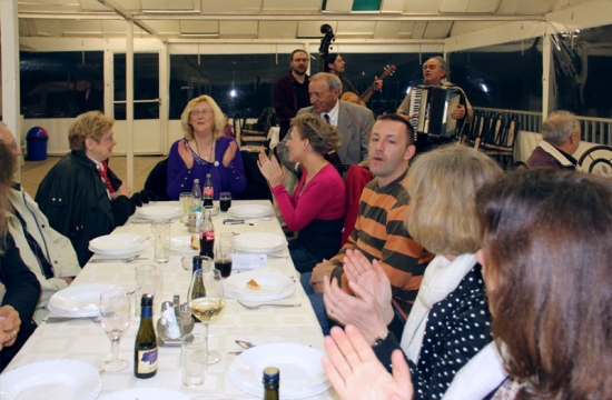 Participants sit around the dinner table in the restaurant and clap their hands while traditional musicians play instruments in the background.