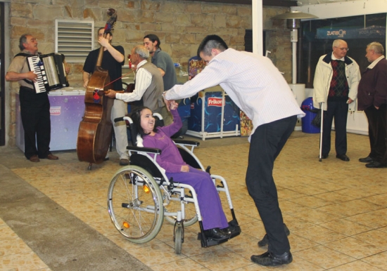 A young man and a young girl in a wheel chair smile and dance together.