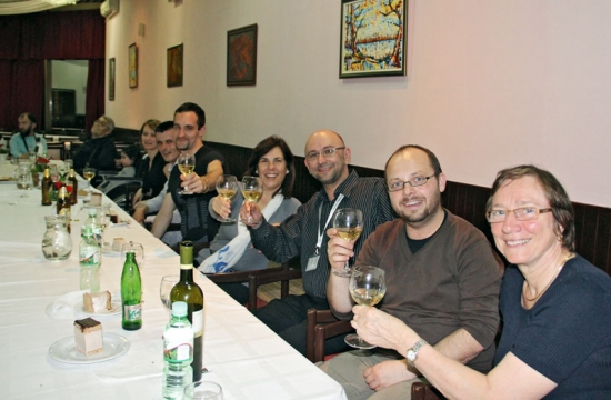 Participants and organizers sit at long tables and raise their wine glasses while smiling for the photo.