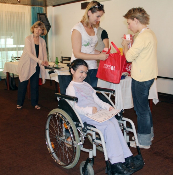 Miroslava Mima Ivanović holds a certificate and smiles broadly while Bojana and Marina Mitrović exchange a red bag with the York University logo on it. Marcia Rioux is in the background.