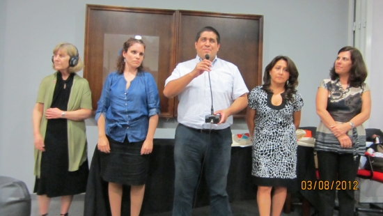 Marcia Rioux, Verónica González, Jose Viera, Ana Lucia Arellano and Paula Pinto stand in a row during closing ceremony. Jose Viera is speaking to the larger group. 