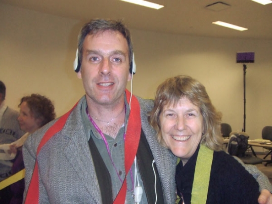 Marcia Rioux (right) and a participant have their photo taken. It is a close up shot, depicting them with Melaine Moore in the background.